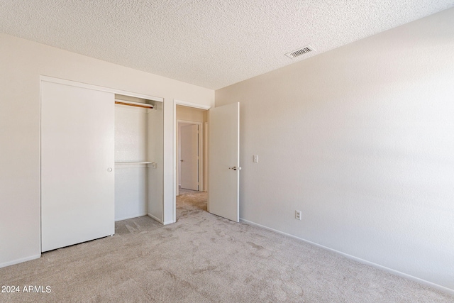 unfurnished bedroom with a textured ceiling, a closet, and light colored carpet