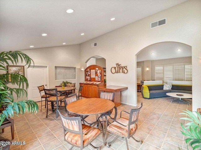 dining space featuring arched walkways, visible vents, lofted ceiling, and light tile patterned floors