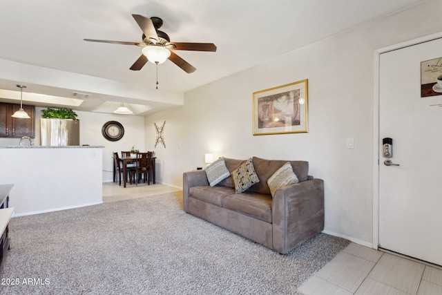 living area featuring ceiling fan, light tile patterned floors, light carpet, and baseboards