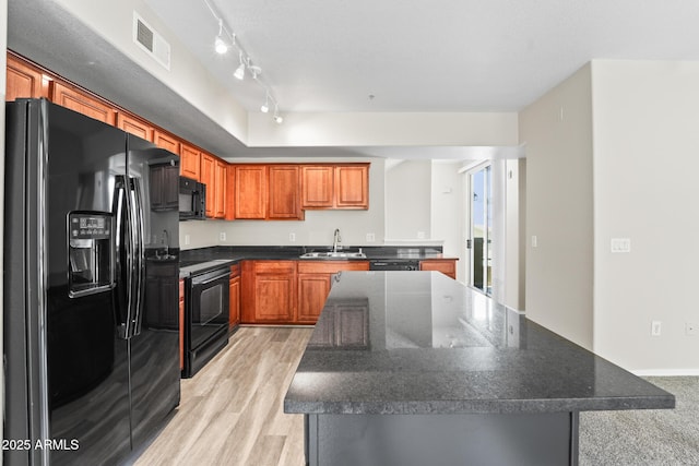 kitchen with a sink, visible vents, light wood-type flooring, a center island, and black appliances