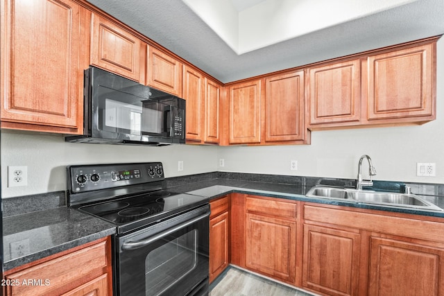 kitchen featuring light wood finished floors, dark countertops, brown cabinets, black appliances, and a sink