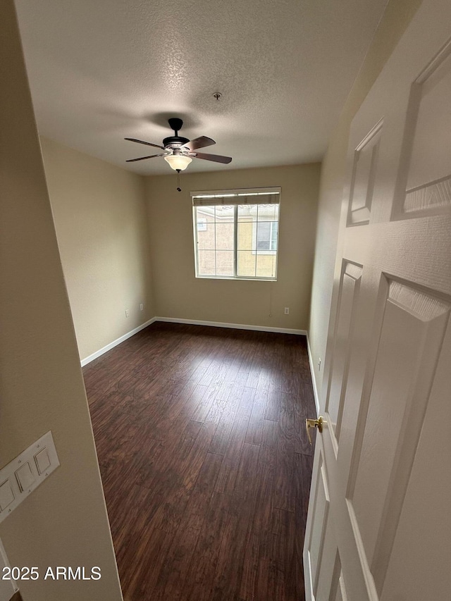 empty room with a textured ceiling, ceiling fan, dark wood finished floors, and baseboards