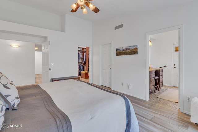 bedroom featuring light wood finished floors, baseboards, visible vents, ceiling fan, and a walk in closet