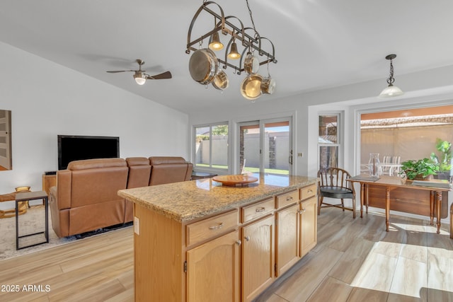 kitchen featuring light stone counters, a kitchen island, vaulted ceiling, hanging light fixtures, and light wood finished floors