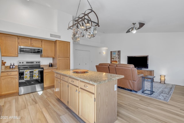 kitchen featuring visible vents, a kitchen island, appliances with stainless steel finishes, light stone counters, and light wood-style floors