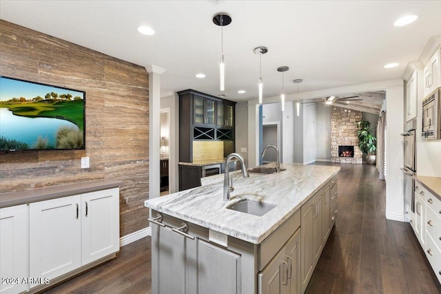 kitchen with dark hardwood / wood-style floors, hanging light fixtures, a large fireplace, and an island with sink