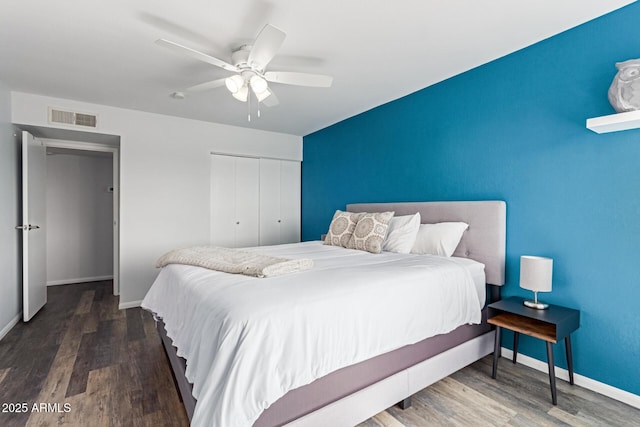 bedroom with ceiling fan, wood finished floors, visible vents, baseboards, and a closet