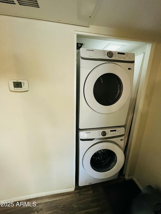 laundry room with stacked washer / drying machine, laundry area, baseboards, and wood finished floors