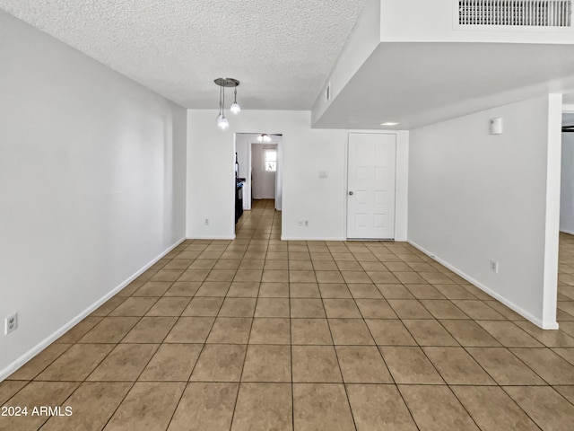 empty room with light tile patterned floors, a chandelier, and a textured ceiling