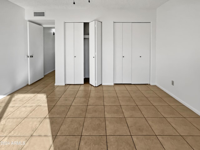 unfurnished bedroom with light tile patterned floors and two closets