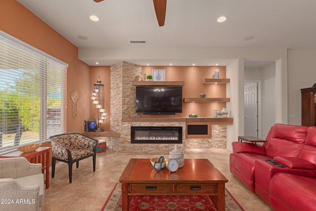 living room featuring light tile patterned floors, a stone fireplace, and ceiling fan