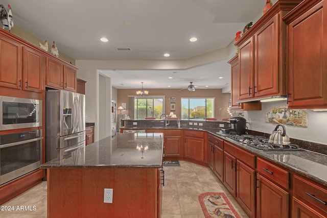 kitchen featuring ceiling fan with notable chandelier, dark stone countertops, appliances with stainless steel finishes, a center island, and kitchen peninsula