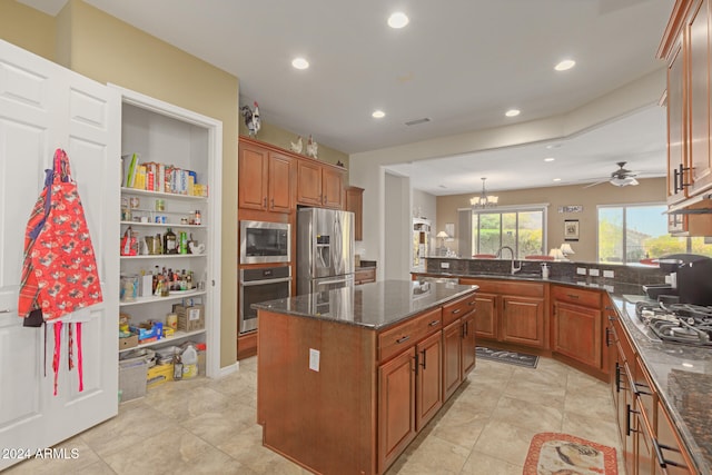 kitchen with a kitchen island, appliances with stainless steel finishes, dark stone counters, ceiling fan with notable chandelier, and kitchen peninsula