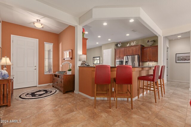 kitchen with kitchen peninsula, appliances with stainless steel finishes, a breakfast bar, and beam ceiling