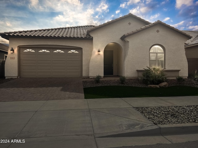 mediterranean / spanish-style home featuring a garage, decorative driveway, a tile roof, and stucco siding