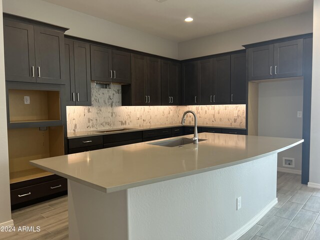 kitchen featuring light countertops, a kitchen island with sink, a sink, and black electric stovetop