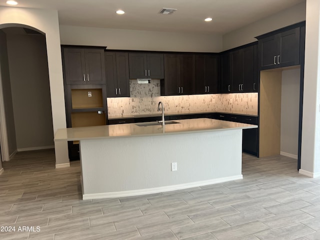 kitchen featuring visible vents, arched walkways, an island with sink, light countertops, and a sink