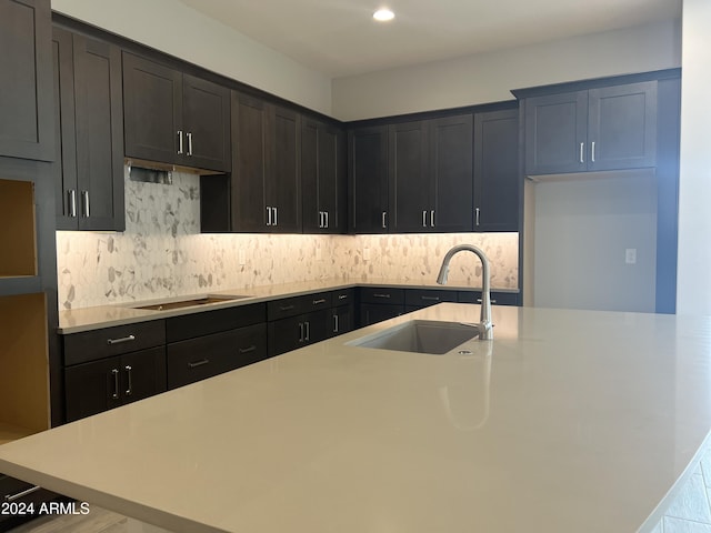 kitchen with tasteful backsplash, light countertops, a sink, and a center island with sink