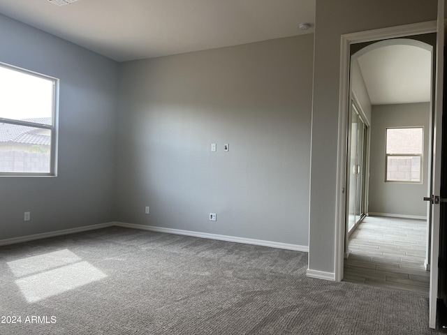 carpeted empty room featuring arched walkways and baseboards