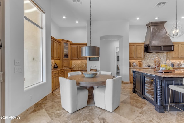 kitchen with visible vents, arched walkways, glass insert cabinets, light stone counters, and custom exhaust hood