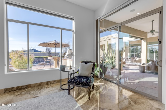 sitting room featuring a sunroom, ceiling fan, baseboards, and a wealth of natural light