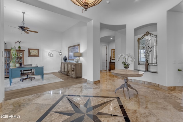 foyer entrance featuring baseboards, arched walkways, a ceiling fan, marble finish floor, and a high ceiling