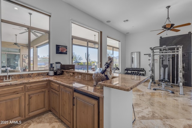 kitchen featuring stone counters, marble finish floor, brown cabinets, a sink, and a peninsula