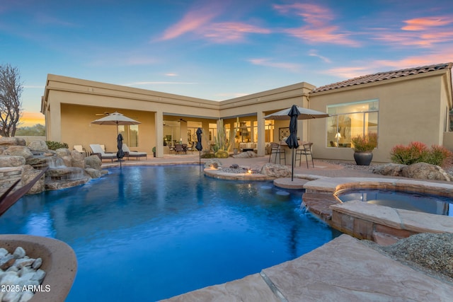 pool at dusk featuring a patio and a pool with connected hot tub