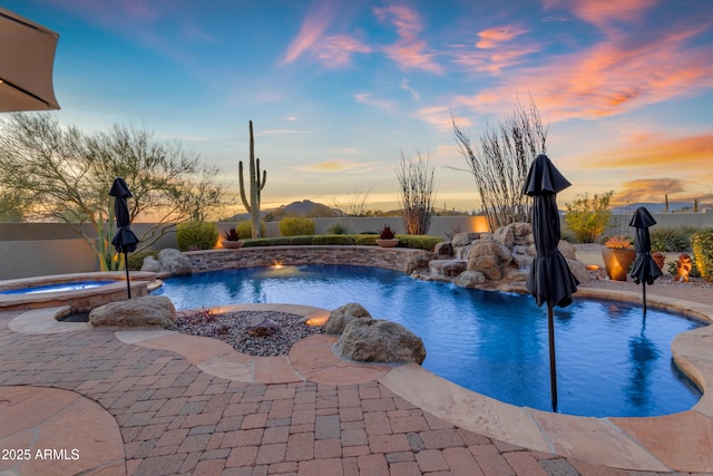 pool at dusk with a fenced in pool, a patio area, fence, and an in ground hot tub