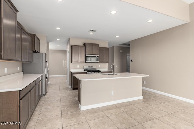 kitchen with dark brown cabinets, stainless steel appliances, sink, light tile patterned floors, and an island with sink