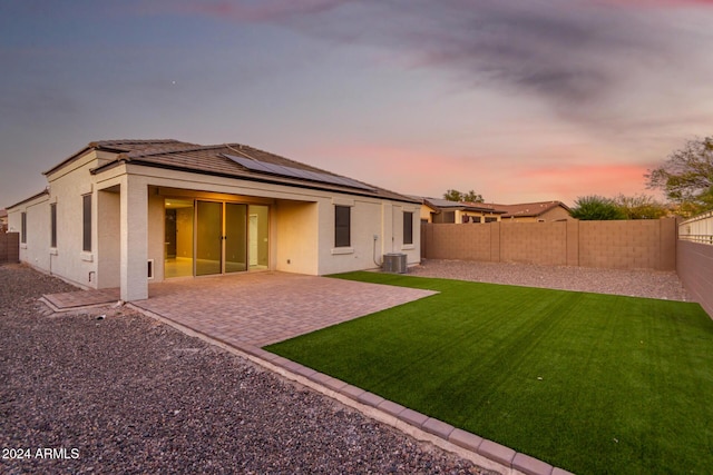 back house at dusk with a patio area, a yard, central AC unit, and solar panels