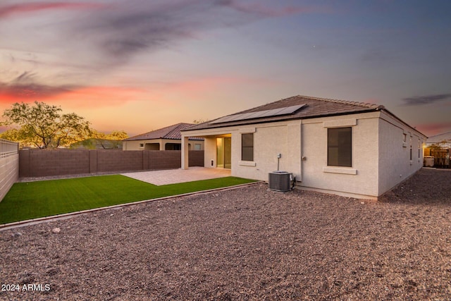 back house at dusk with a yard, a patio, central AC unit, and solar panels