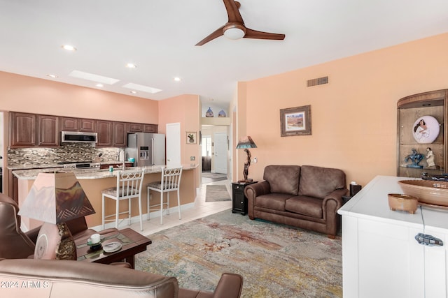 tiled living room with sink, ceiling fan, and a skylight