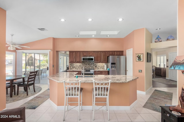 kitchen featuring a kitchen breakfast bar, an island with sink, stainless steel appliances, lofted ceiling with skylight, and ceiling fan