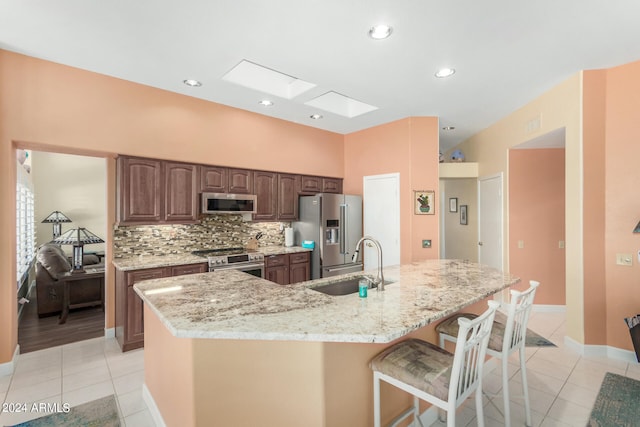 kitchen with a kitchen breakfast bar, a large island with sink, premium appliances, a skylight, and sink