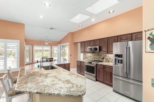 kitchen featuring ceiling fan, vaulted ceiling with skylight, sink, a kitchen island with sink, and appliances with stainless steel finishes