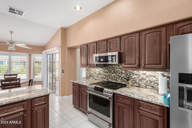 kitchen with vaulted ceiling, light stone counters, backsplash, stainless steel appliances, and ceiling fan