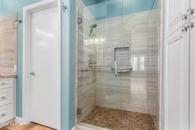 bathroom with a notable chandelier, wood-type flooring, a shower with shower door, and vanity