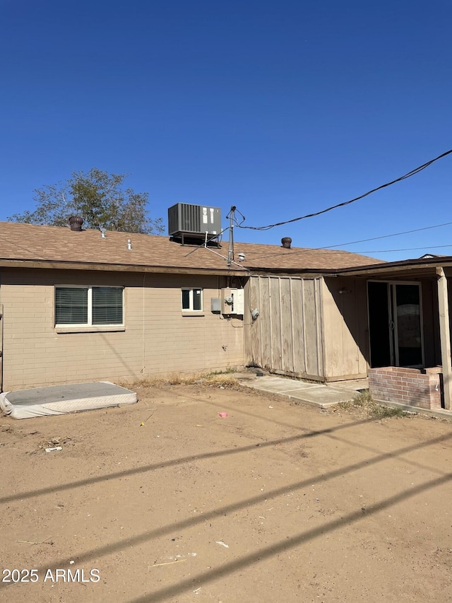 back of house featuring brick siding, roof with shingles, and central AC unit