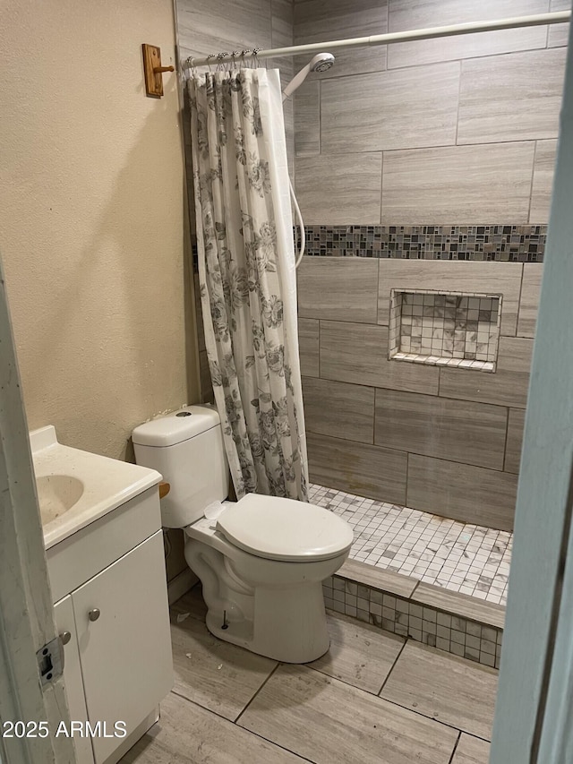 bathroom featuring toilet, a stall shower, a textured wall, and vanity