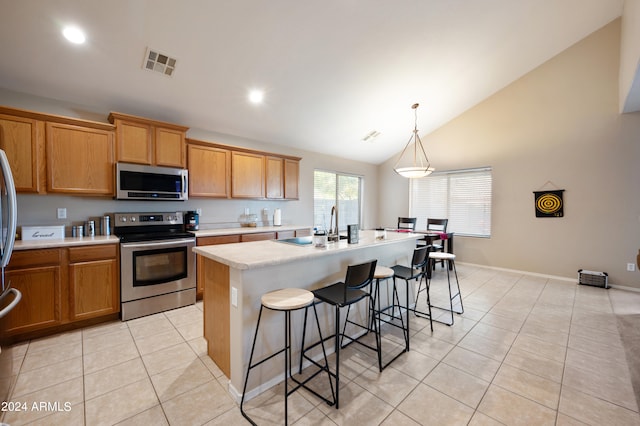 kitchen featuring lofted ceiling, light tile patterned flooring, hanging light fixtures, appliances with stainless steel finishes, and a center island with sink