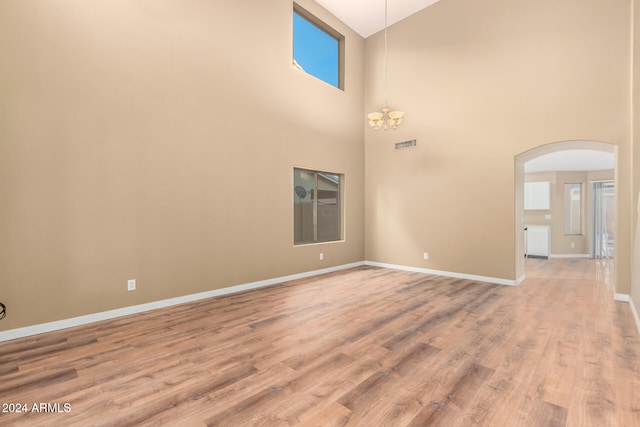 spare room featuring an inviting chandelier, a towering ceiling, and hardwood / wood-style flooring