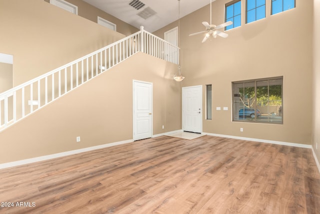 unfurnished living room featuring ceiling fan, a towering ceiling, and wood-type flooring