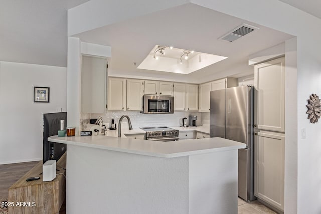 9450 E Becker Ln Unit 1046, Scottsdale, AZ 85260 - kitchen featuring stainless steel appliances, a tray ceiling, a peninsula, light countertops, and decorative backsplash