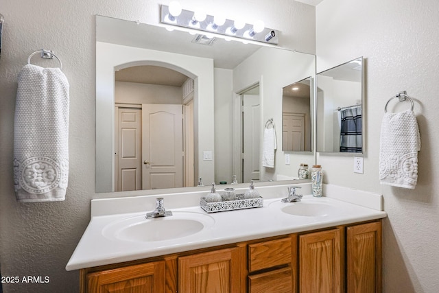 bathroom with a textured wall, visible vents, a sink, and double vanity