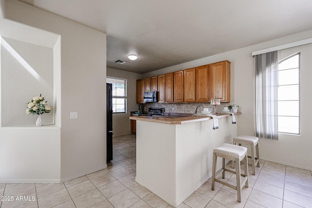 kitchen featuring light tile patterned floors, a breakfast bar, visible vents, and black appliances