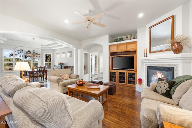 living room featuring dark hardwood / wood-style flooring, a tray ceiling, ceiling fan with notable chandelier, and decorative columns