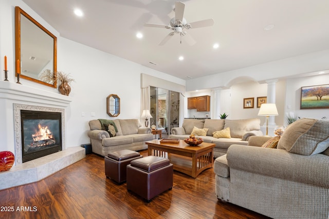 living room featuring dark wood-type flooring, ceiling fan, and ornate columns