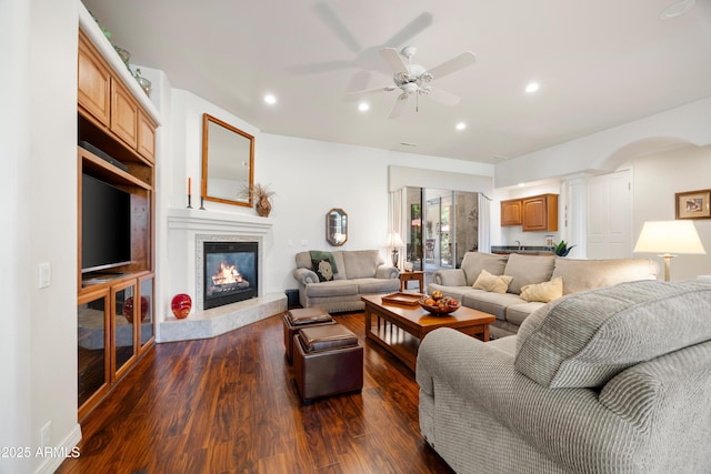 living room with a high end fireplace, dark wood-type flooring, and ceiling fan