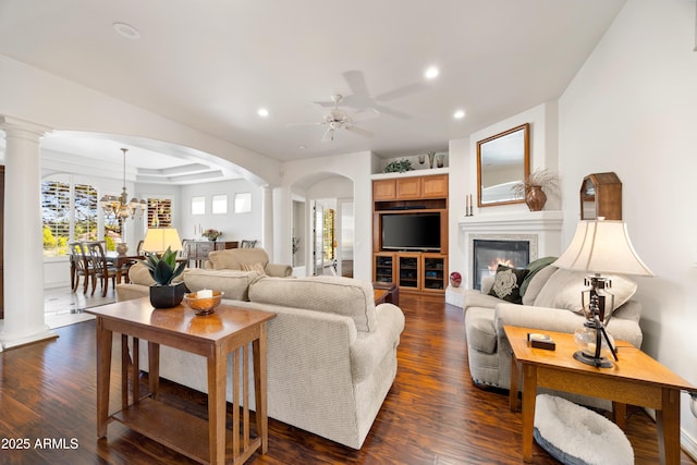 living room featuring ceiling fan, a tray ceiling, dark hardwood / wood-style floors, and decorative columns